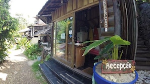 A wooden building with a reception area, a sign reading "Recepção," and a potted plant in front.