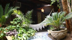 Un sendero de baldosas que conduce a una puerta de madera, rodeado de plantas en macetas y una hamaca colgante.