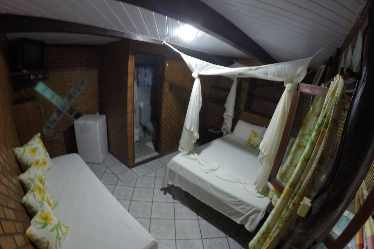Una habitación con cama, un banco, televisor y ventana.