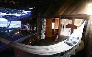 A hammock bed with a view of the ocean, wooden walls, and a small room with a bed and a nightstand.