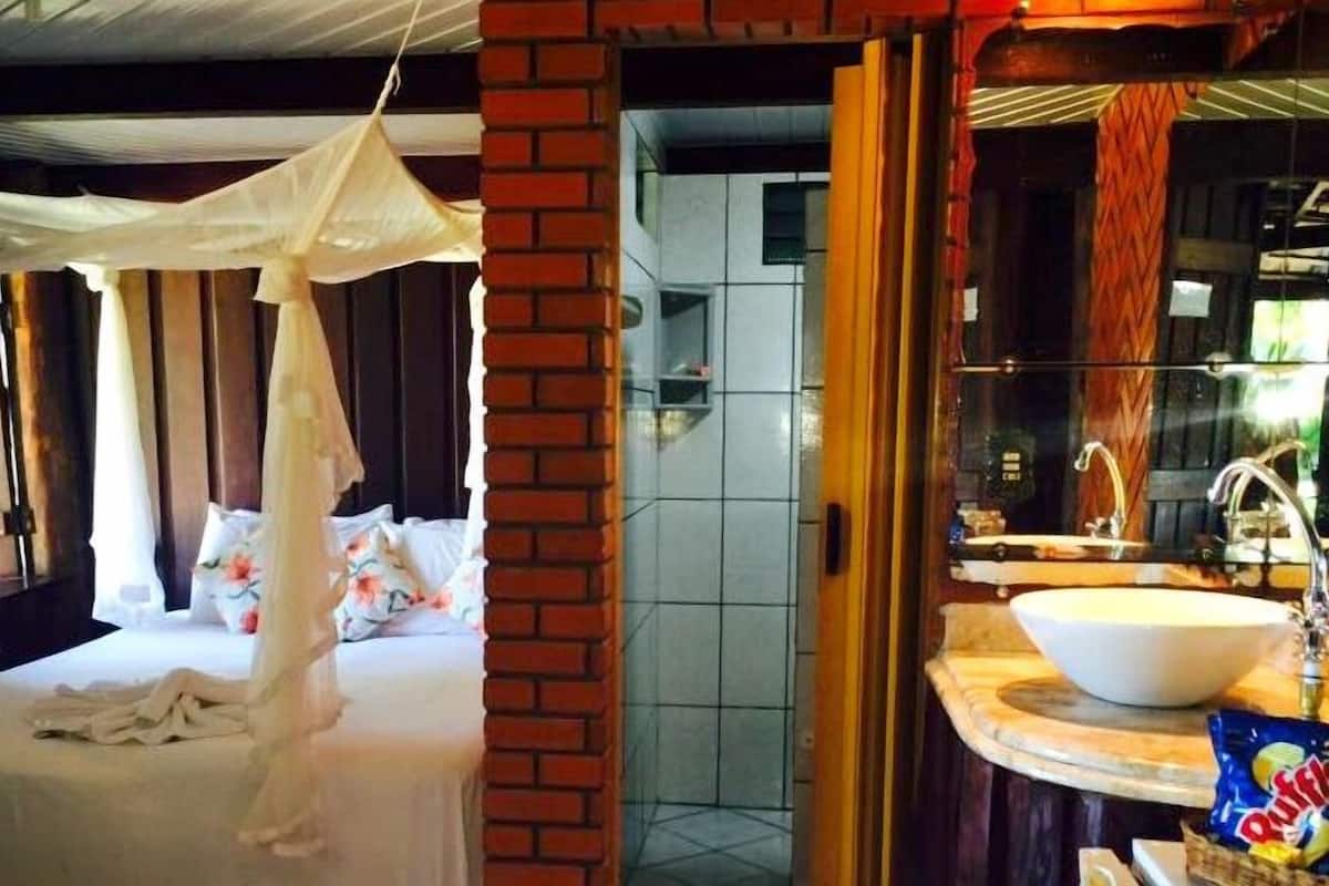 Una habitación con una cama bajo un dosel, un baño con lavabo y espejo, y una pared de ladrillo.