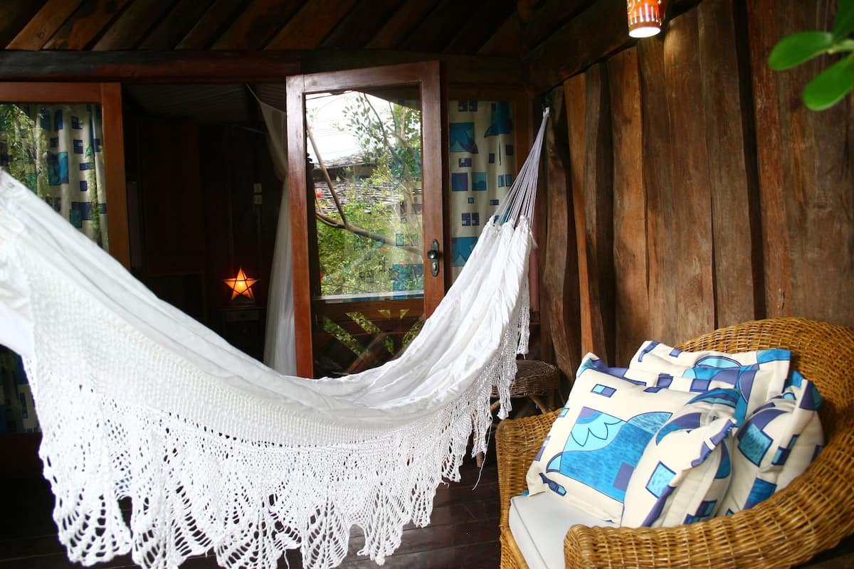 Una hamaca suspendida sobre una silla de mimbre con cojines estampados, una puerta de madera y una lámpara con forma de estrella.
