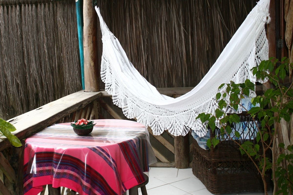 Un pequeño patio con una mesa cubierta por un mantel a rayas, una hamaca y una cesta de mimbre con una planta.