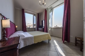 A bedroom with a bed, a nightstand, a TV, and large windows with curtains. - I Terzi di Siena (Siena)