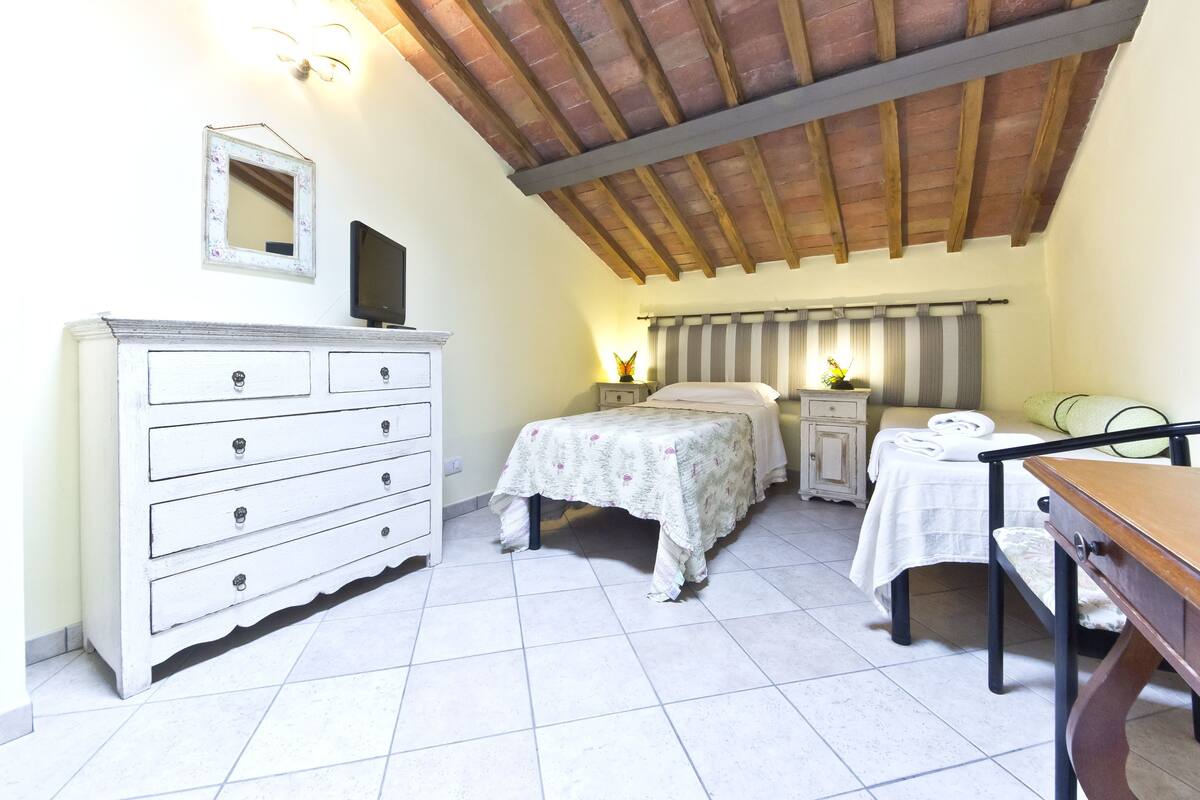 Um quarto com cama, penteadeira, mesa de cabeceira, mesa e cadeira.
