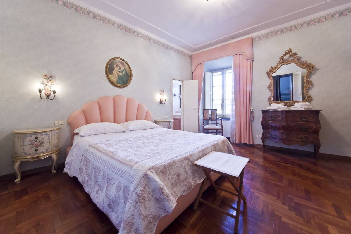 Quarto com uma cama grande, cômoda de madeira, penteadeira com espelho e uma mesinha.