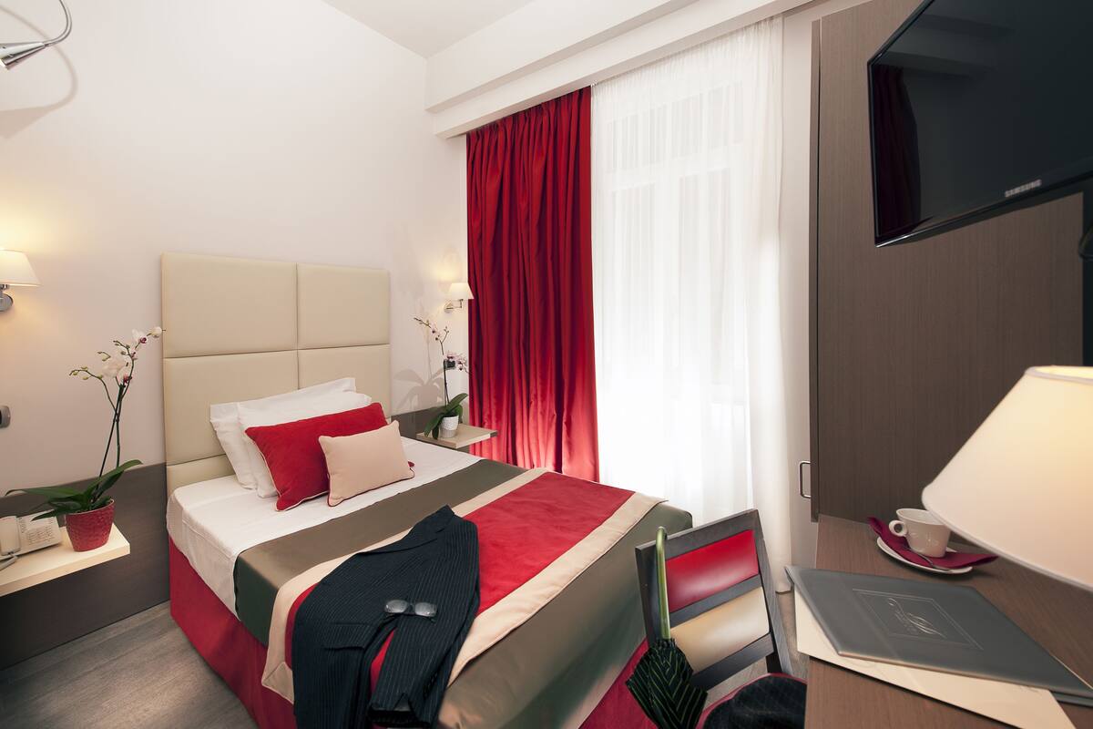 A hotel room with a bed, a desk, a chair, a TV, and a window with curtains.