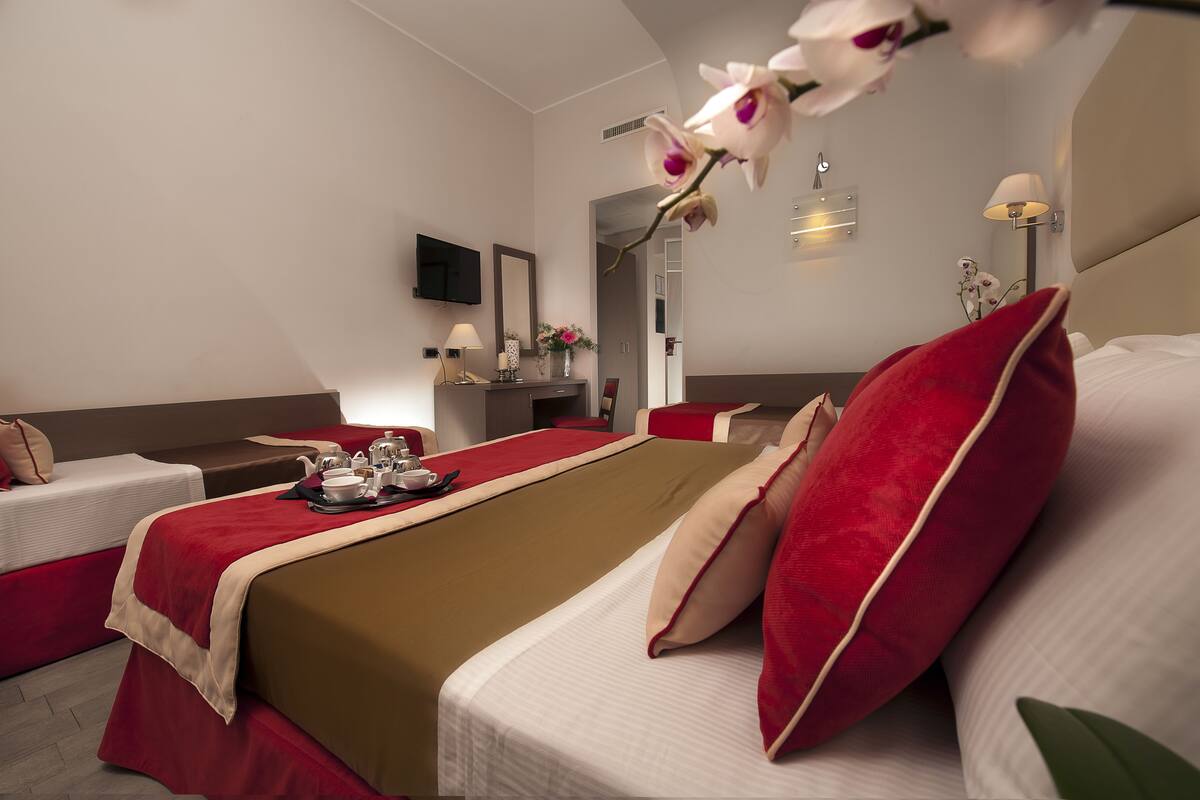 A hotel room with two beds, a TV, a mirror, a bedside table with a lamp, and a vase with flowers.