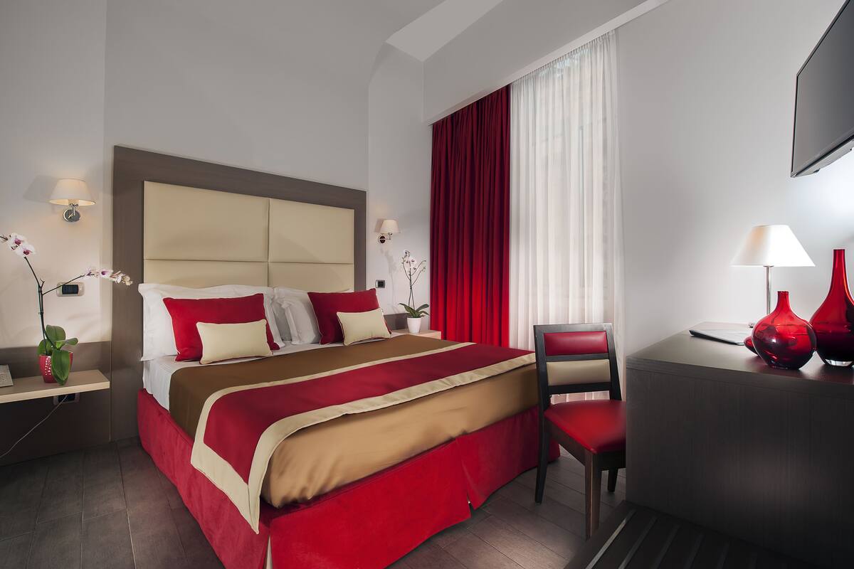 A hotel room with a large bed, a desk, a chair, and a TV.