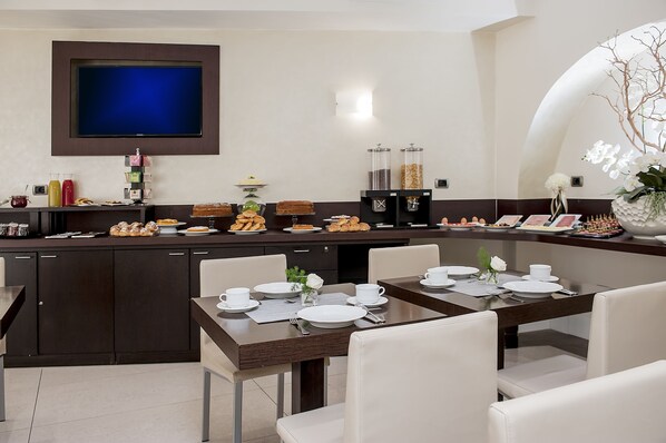 A modern kitchen with a flat-screen TV, breakfast bar, and buffet with various food items. - Demetra Hotel (Rome)