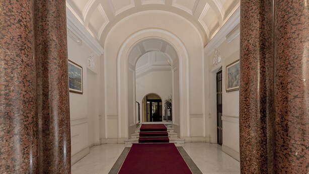 Un gran pasillo con columnas de mármol, alfombra roja y un diseño de techo clásico.