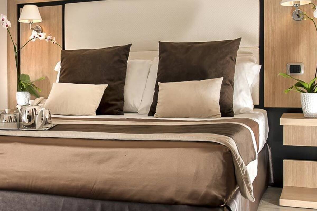 A modern hotel room with a large bed, bedside tables, a mirror, and a small desk with a lamp.