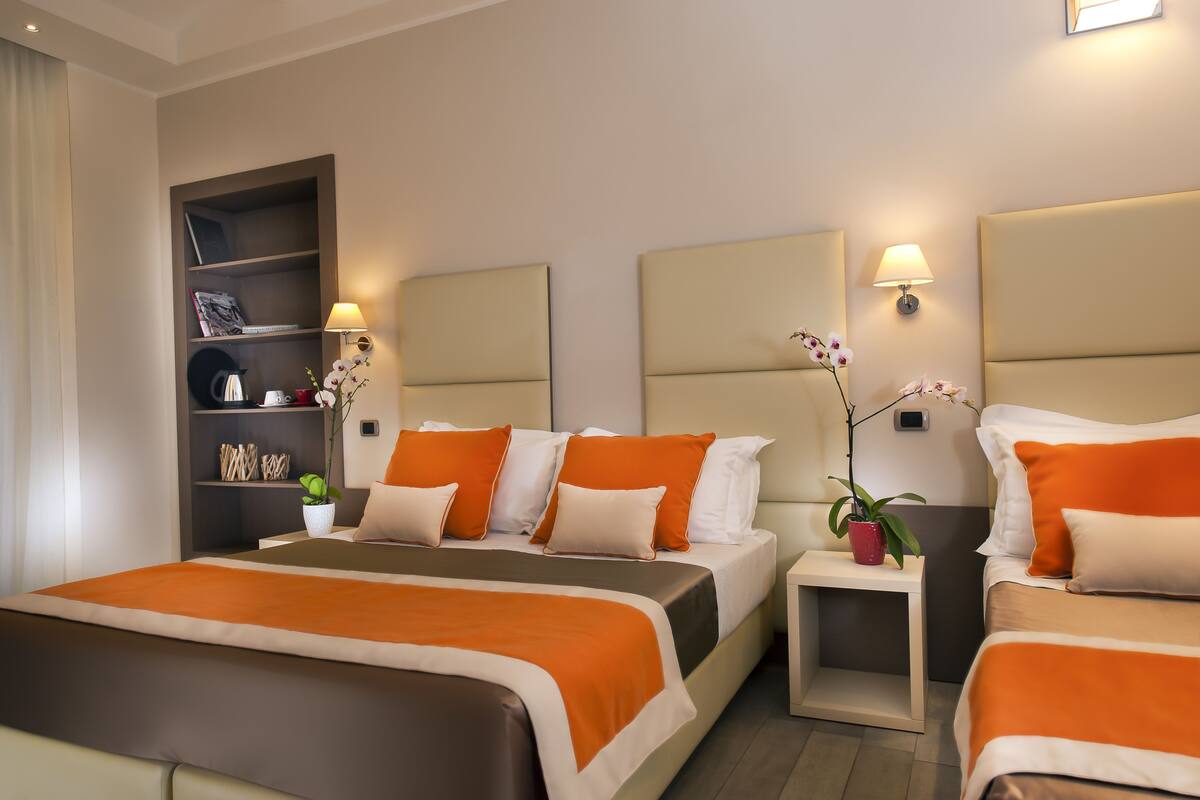 A hotel room with two beds, a bookshelf, and two bedside tables with lamps.