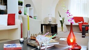 Una sala de estar moderna con un sofá blanco, cojines rojos, una mesa de centro con libros, un juego de ajedrez y objetos decorativos.