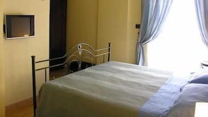 A bedroom with a bed, a wardrobe, a small TV, and a window with curtains. - Residenza Sveva (Bari)
