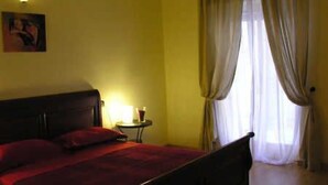 A room with a bed, a bedside table with a lamp, and a window with curtains. - Residenza Sveva (Bari)