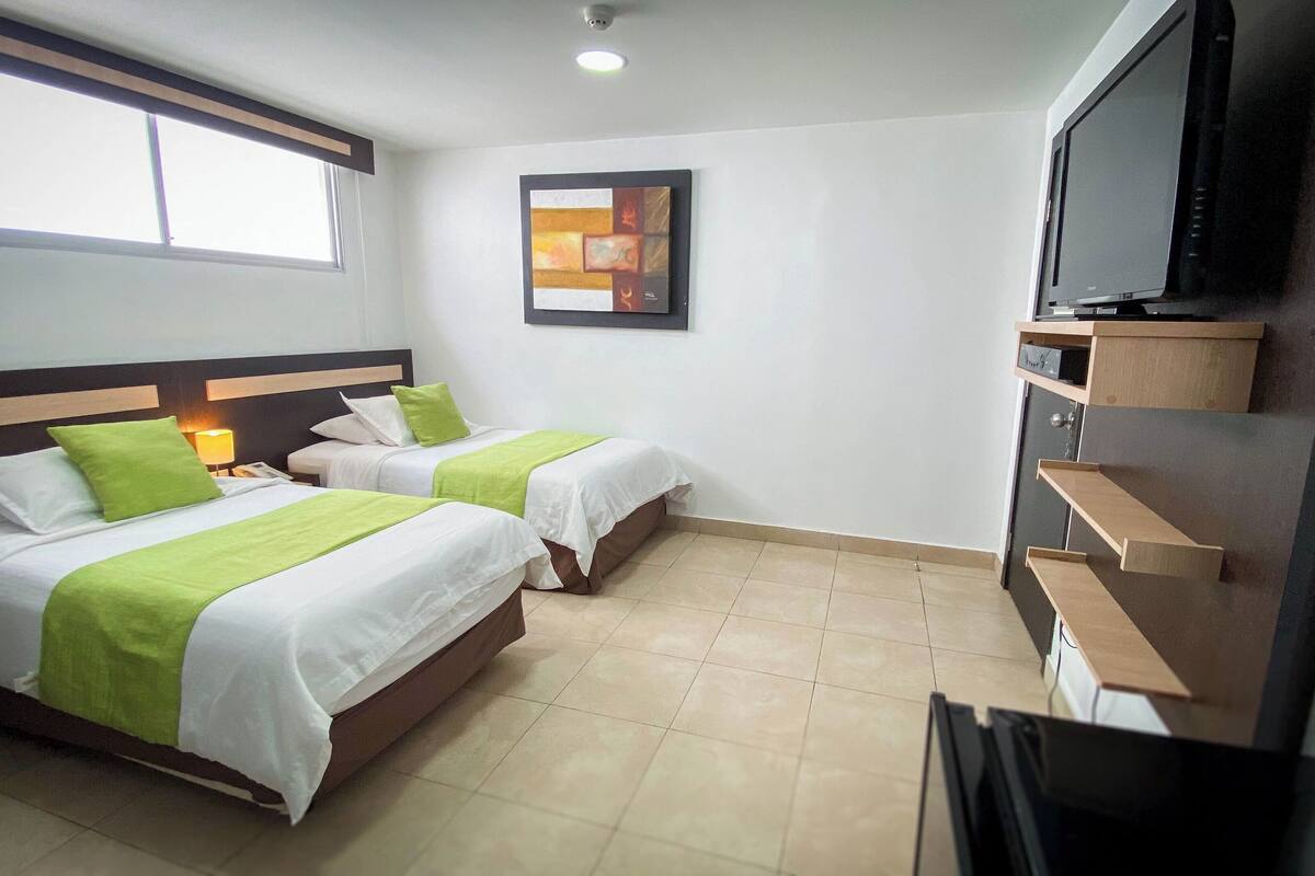 Habitación de hotel con dos camas, un televisor y un cuadro en la pared.