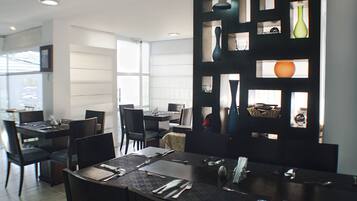 A modern dining area with multiple tables and chairs, a decorative wall with vases, and a large window providing natural light.