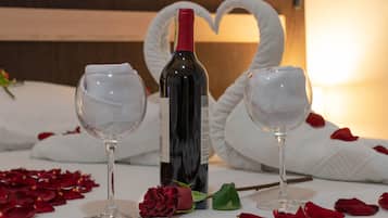 Una mesa con dos copas de vino, una botella, una rosa y toallas con forma de corazón.