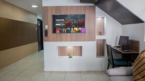 Eine moderne Lobby mit einem Flachbildfernseher, der einen Film zeigt, einem Empfangstresen, einem Computer und einer gemütlichen Sitzecke.