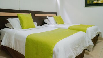 Ein Hotelzimmer mit zwei Betten, jeweils mit weißer Bettwäsche und grünen Akzenten.