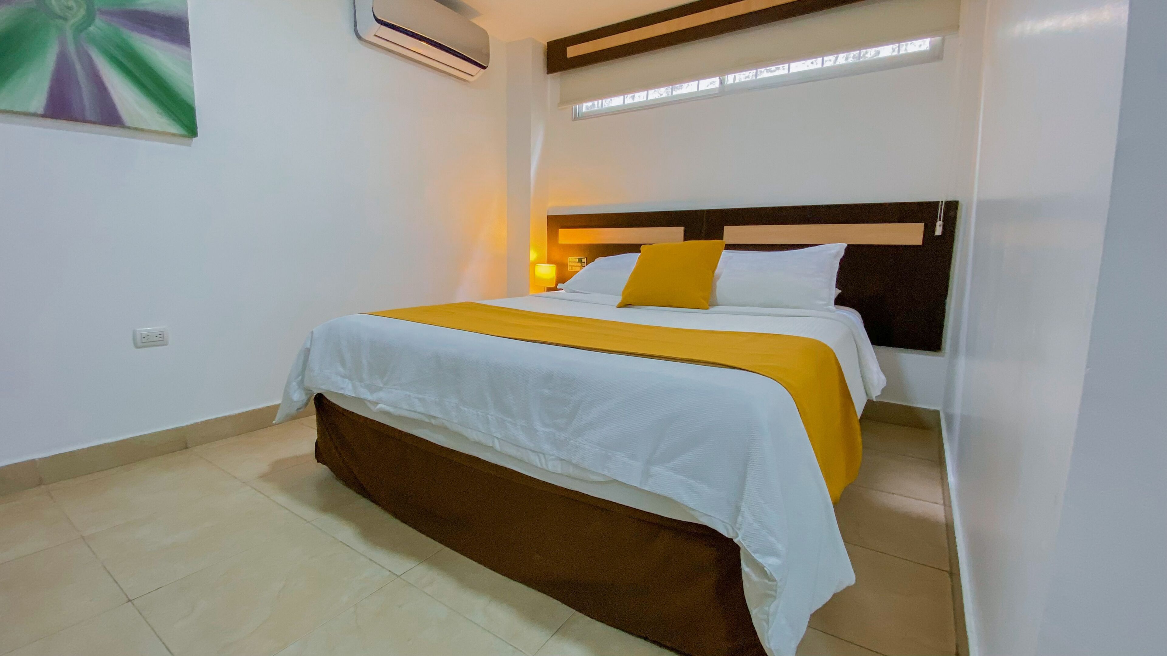 A neatly made bed with a white and yellow bedspread, a brown headboard, and a single yellow pillow.