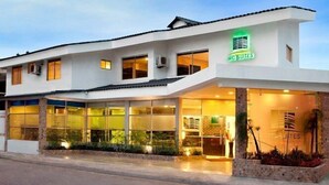 Ein modernes Hotel mit heller Fassade, großen Glasfenstern und einem grünen Schild, das es als McCutes Hotel kennzeichnet.