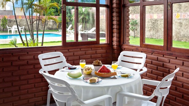 A dining area with a brick wall, white plastic chairs, and a table set with food and drinks. - CLH Suites Bonito Sul - Hostel (Bonito)