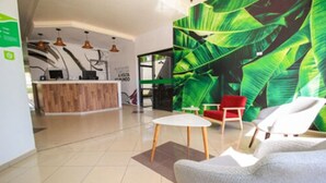 A modern lobby with a wooden reception desk, a green leafy wall mural, and a seating area with a small round table and two chairs. - CLH Suites Bonito Sul - Hostel (Bonito)