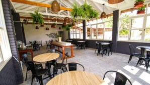An indoor dining area with tables and chairs, large windows, and hanging plants. - CLH Suites Bonito Sul - Hostel (Bonito)