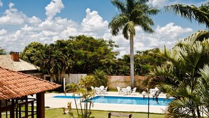 A pool area with a palm tree, white lounge chairs, and a wooden bench. - CLH Suites Bonito Sul - Hostel (Bonito)