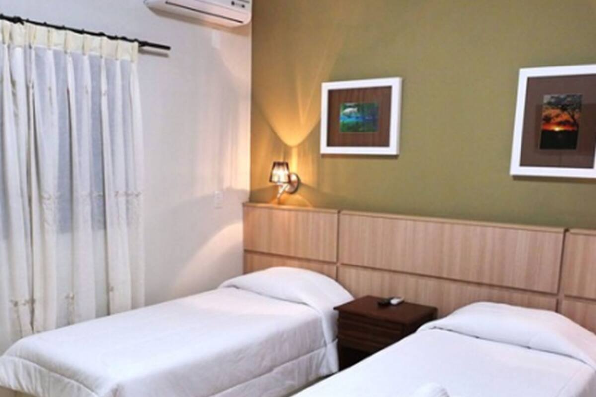 Una habitación de hotel con dos camas individuales, una mesita de noche, una lámpara y aire acondicionado instalado en la pared.