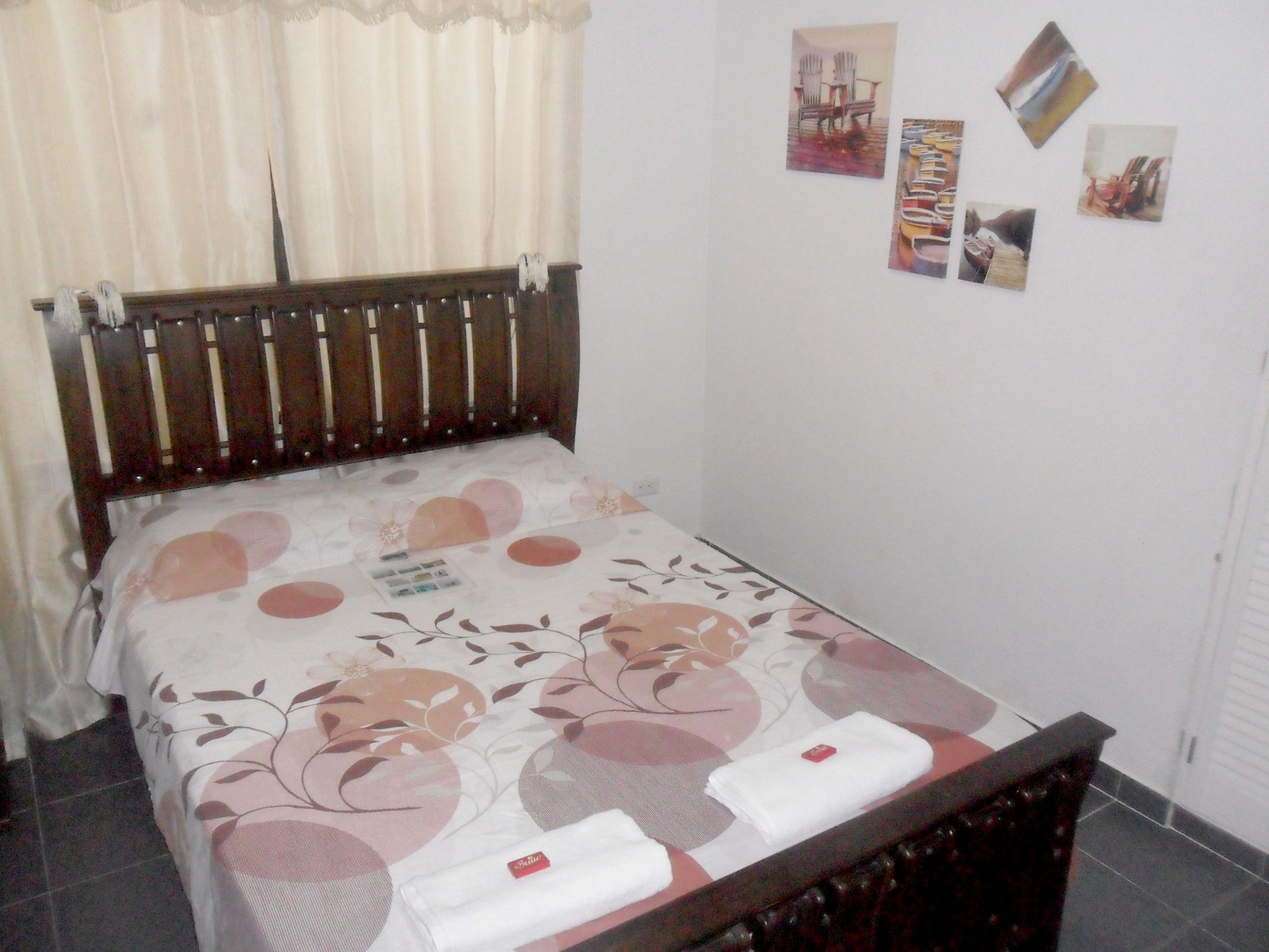 A neatly made bed with a floral bedspread, a wooden headboard, and a set of towels on the side.