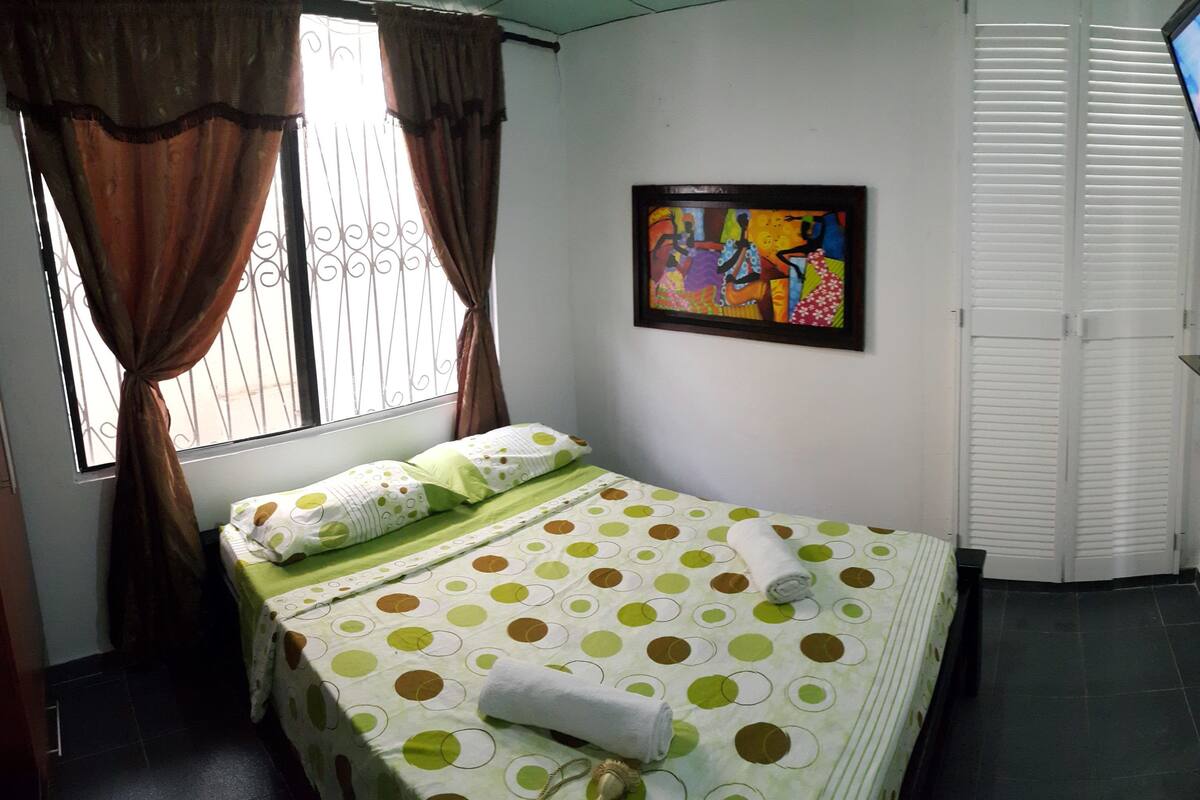 A bedroom with a bed, curtains, a painting, a television, and a window.