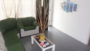 Un salon avec un canapé vert, une table basse en verre agrémentée d’objets décoratifs et une porte avec un rideau.