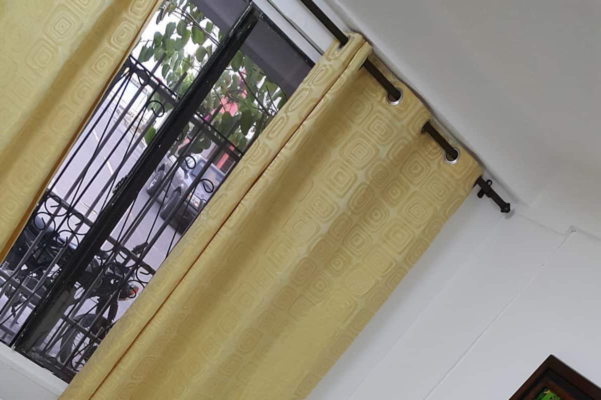 A room with a bed, a window with a view of a street and trees, and a painting on the wall.