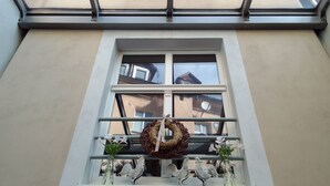 Een raam met een krans, twee metalen haanornamenten en een kleine plant.