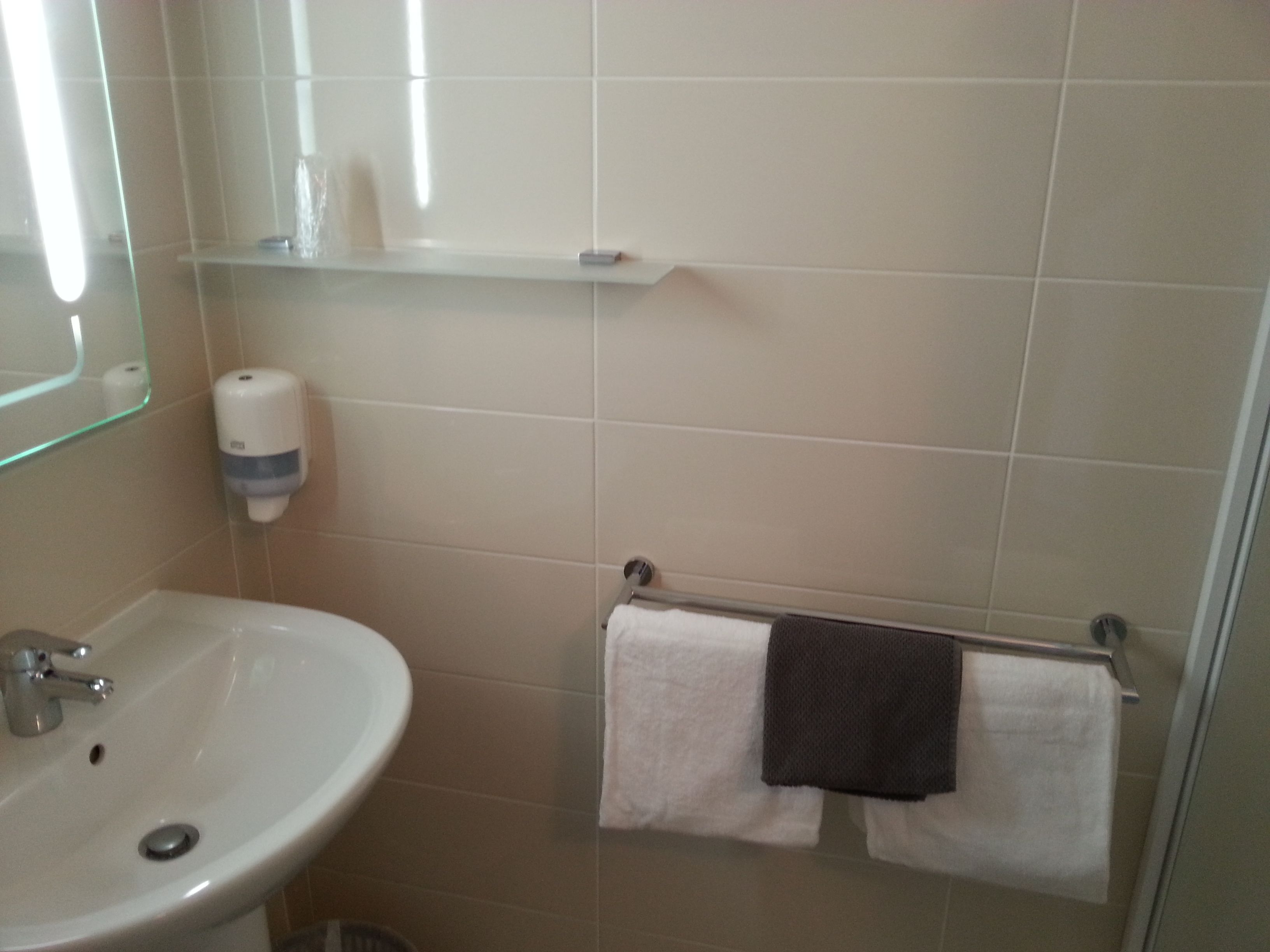 A bathroom with a sink, mirror, towel rack, and soap dispenser.