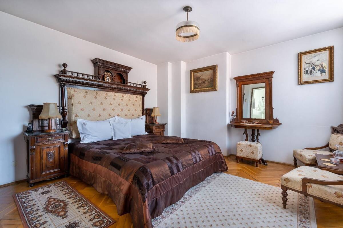 Un dormitorio con una cama grande, un aparador de madera, una mesita de noche, una silla y un espejo.