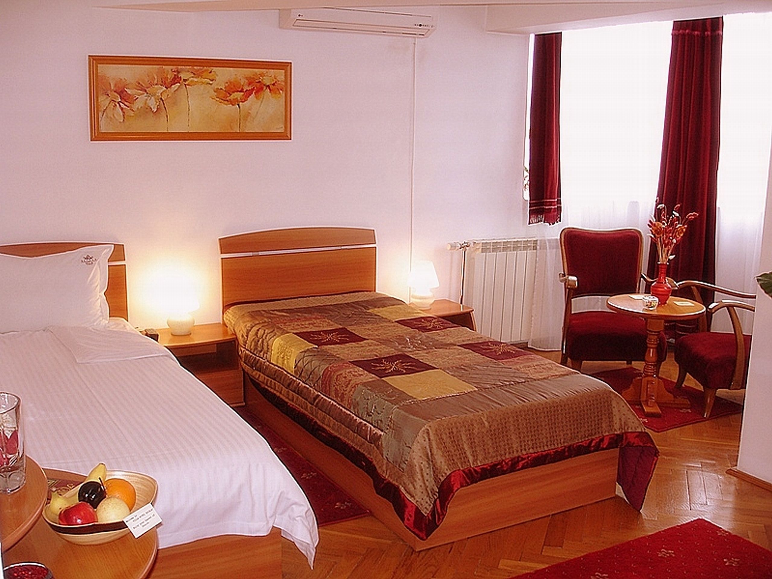 Ein Hotelzimmer mit einem Bett, Nachttischen, einem Sessel, einem kleinen Tisch mit einer Vase und einem Bild an der Wand.