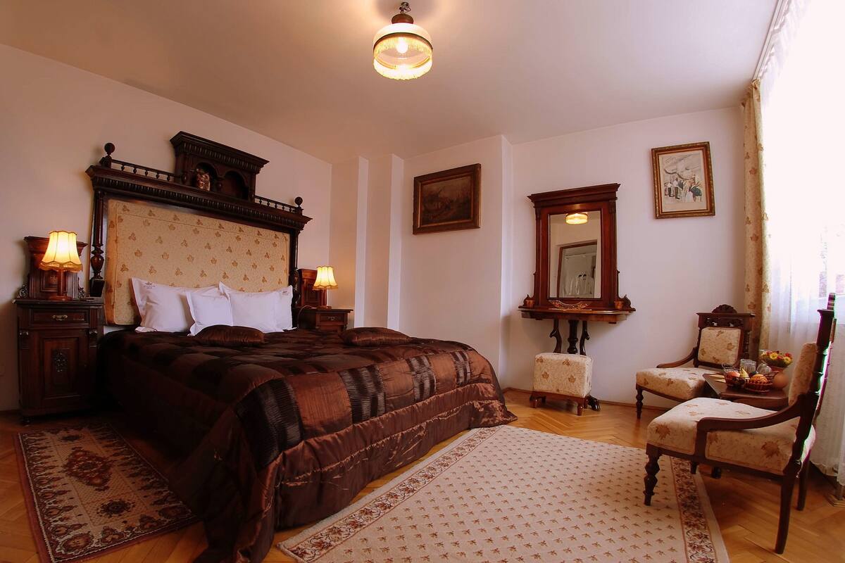 Un dormitorio con una cama grande, dos mesitas de noche con lámparas, una silla, un espejo y una alfombra.