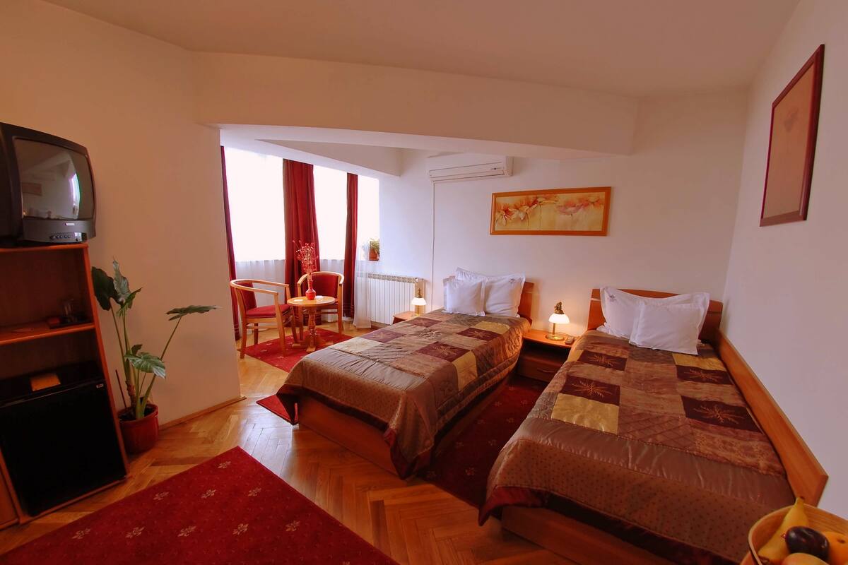 Habitación de hotel con dos camas, televisión, escritorio con silla, alfombra roja y un cuadro en la pared.