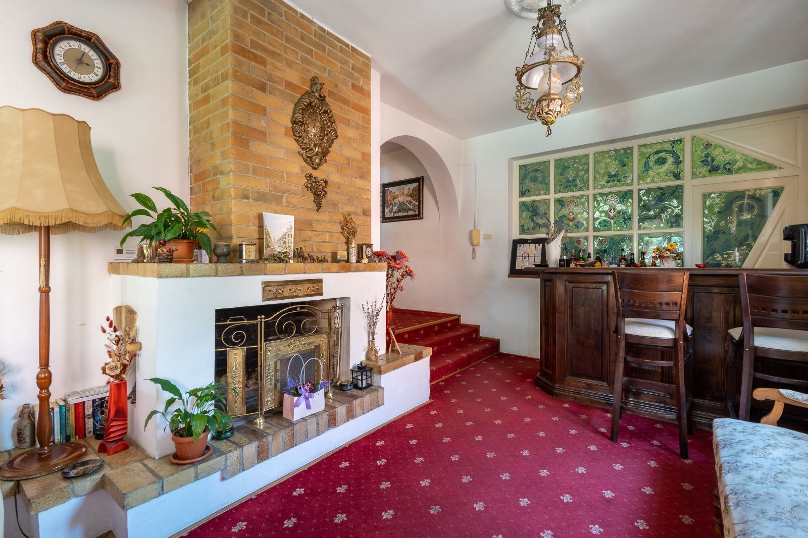 A cozy living room with a fireplace, a dining area with wooden chairs, and a red carpet.