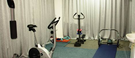 A home gym with exercise equipment including a stationary bike, elliptical, and weight bench.