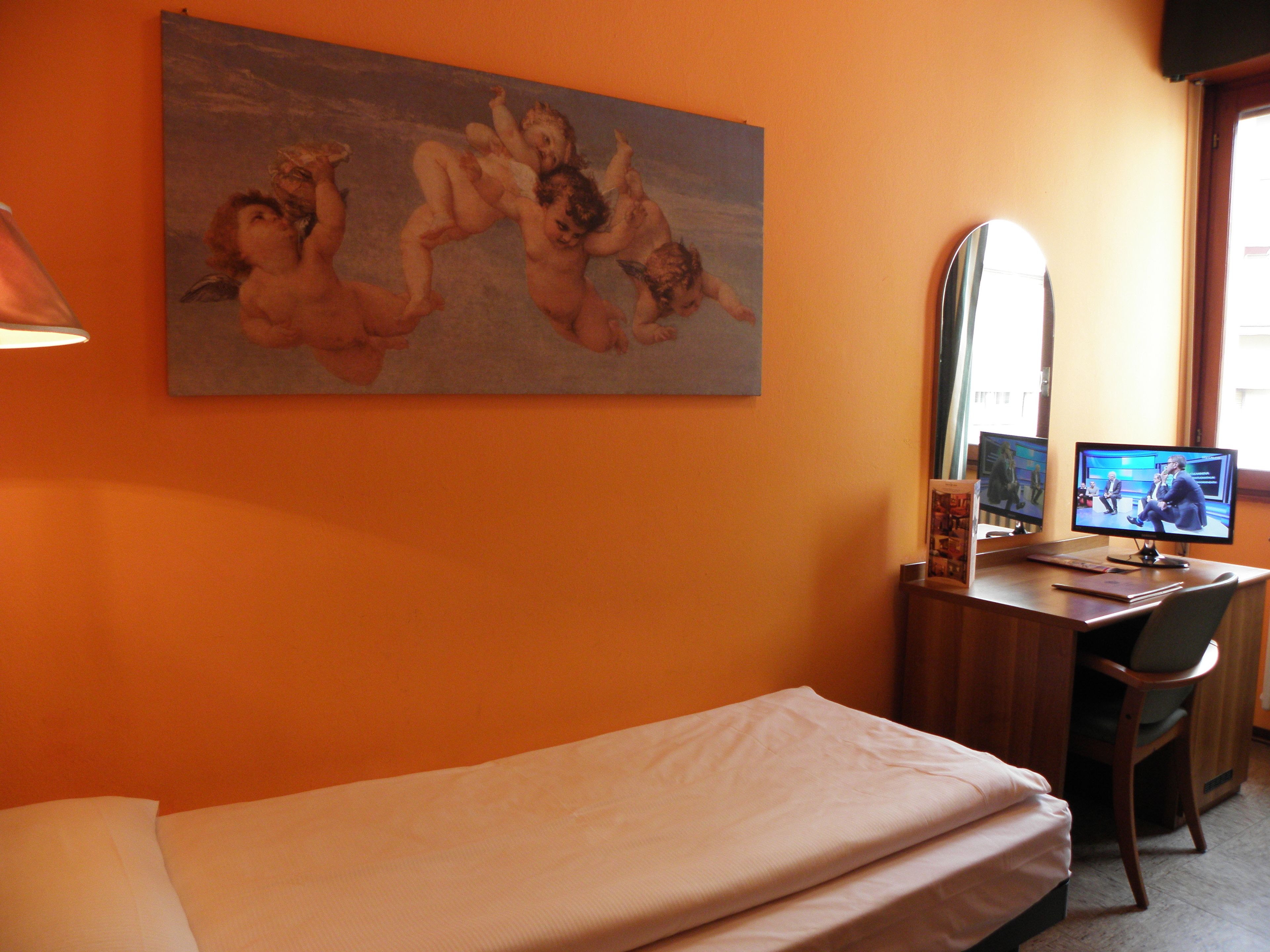 Una camera d'albergo con un letto, una scrivania con un computer, una sedia e un quadro appeso al muro.