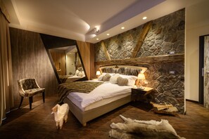 Un dormitorio con pared de piedra, piso de madera, una cama con almohadas, una silla y una mesita de noche con lámpara.