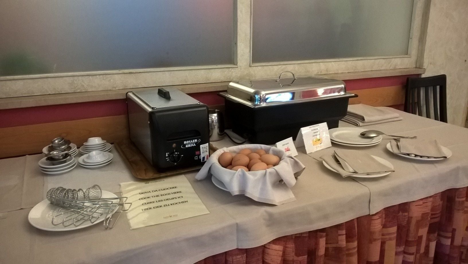 A buffet table with a toaster, a bowl of eggs, and a sign instructing to cook the eggs here.