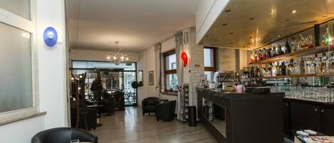 A modern bar area with a wooden counter, shelves of bottles, and a seating area with tables and chairs.