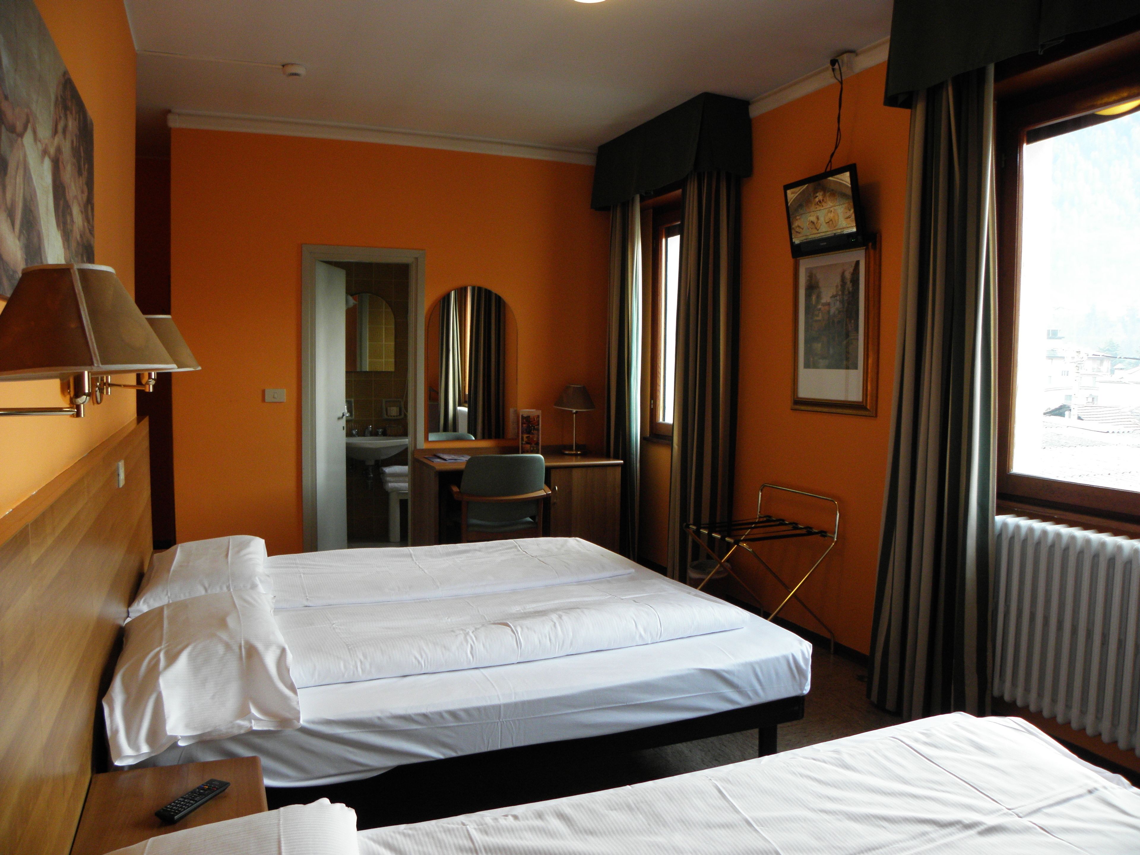 A hotel room with two beds, a desk, a chair, a mirror, a window with curtains, and a television.