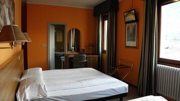 A hotel room with two beds, a desk, a chair, a mirror, a window with curtains, and a television.